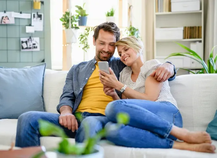 Smiling couple on a sofa checking a phone, showing how CityBiz Portal Now helps people discover nearby services